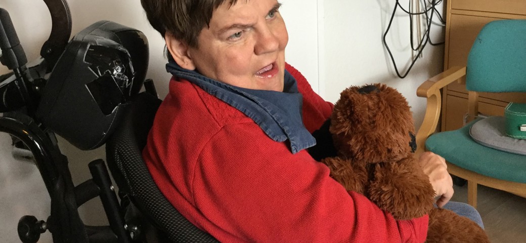 Kvinde sidder i sin kørestol og holder ved en brun bamse