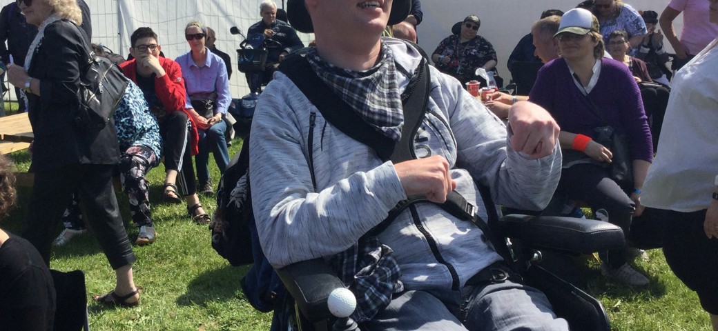 Personer i kørestol sidder og smiler til en festival i solskinsvejr